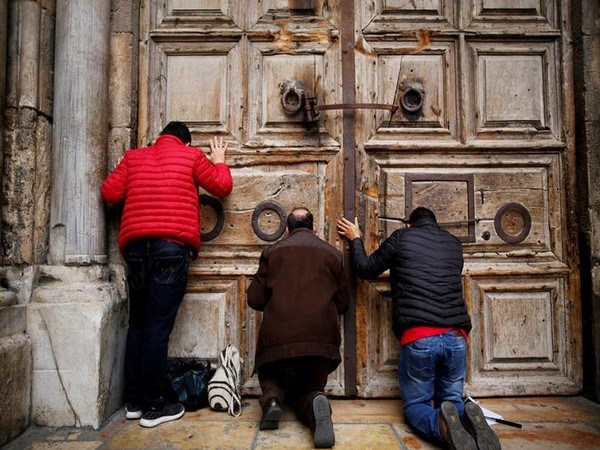 Worshippers kneel and pray in front of the closed doors of the Church of the Holy Sepulchre in Jerusalem's Old City